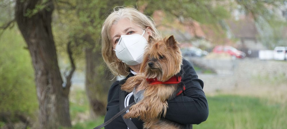 Frau mit Mundschutz hält Hund im Arm
