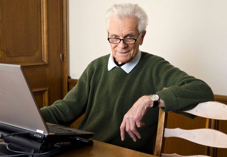 Portr&auml;t von Ernst Brandl, am Schreibtisch sitzend mit aufgeklapptem Laptop vor sich.