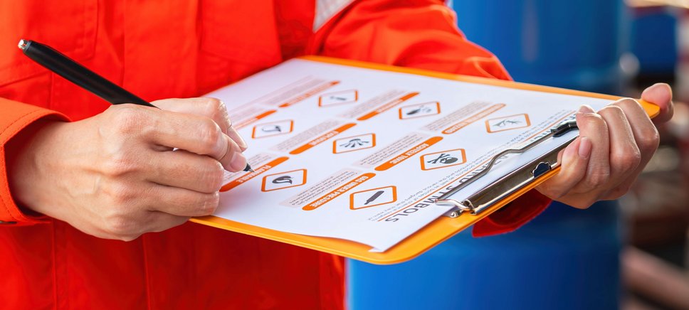 Eine Person in einem orangen Schutzanzug pr&uuml;ft eine Checkliste