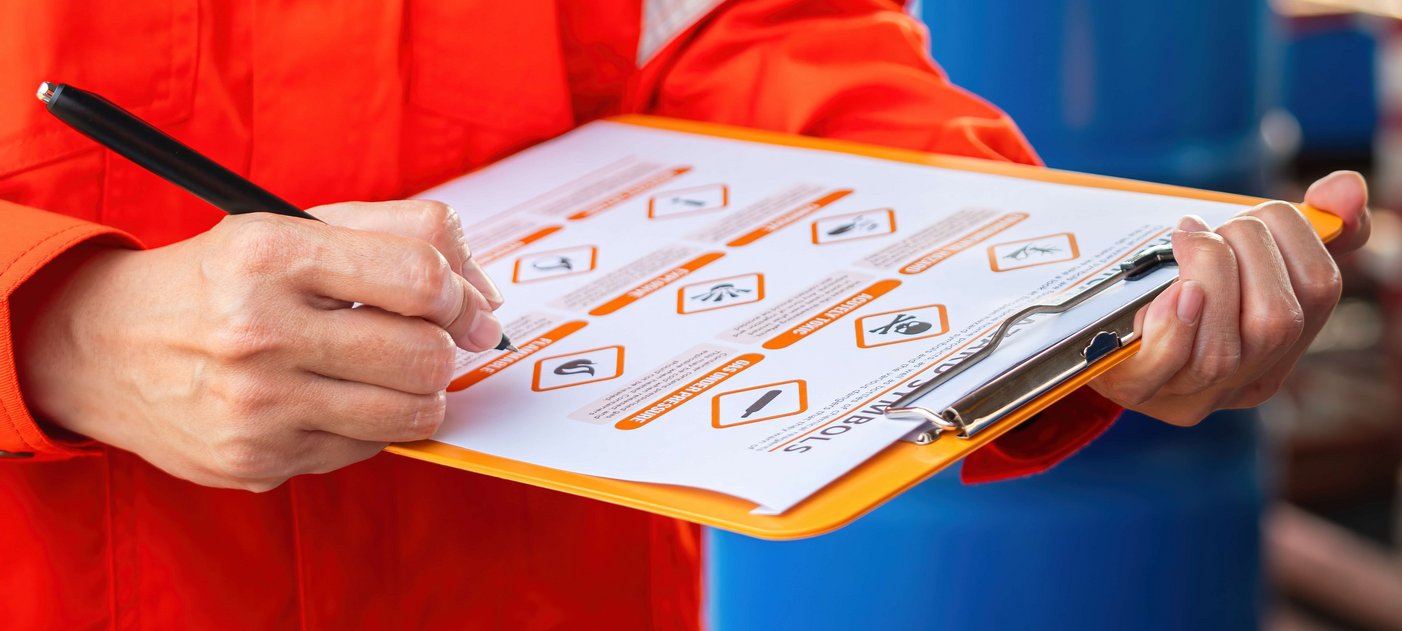 Eine Person in einem orangen Schutzanzug prüft eine Checkliste