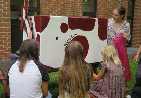 Kinder stehen um eine Kuh aus Karton herum