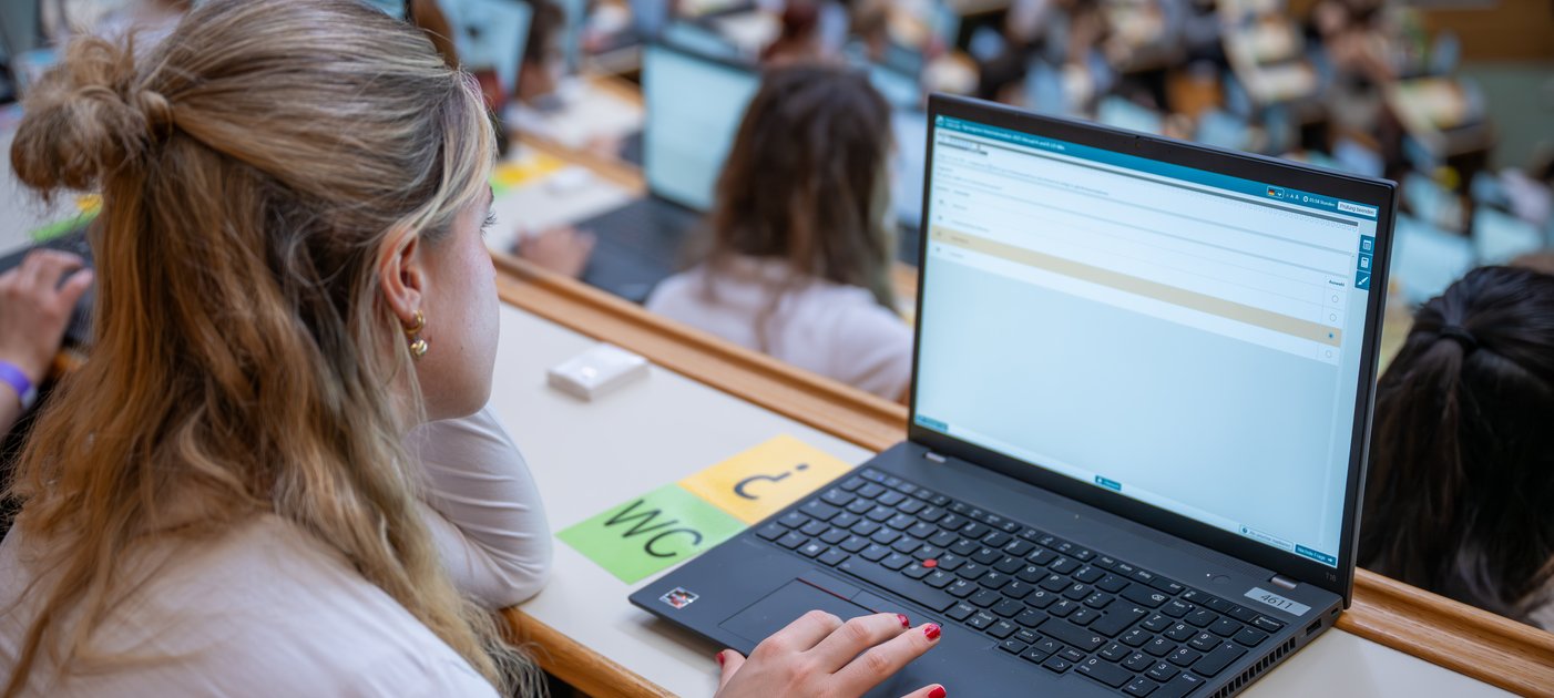 Studentin sitzt vor Laptop in vollem Hörsaal