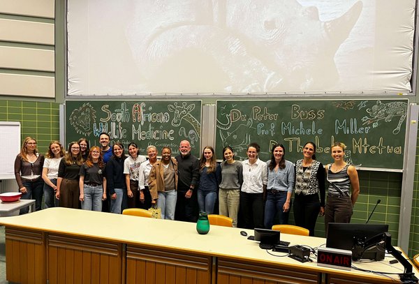 Ein Gruppenfoto aller involvierten Teilnehmer:innen vor der Tafel im Hörsaal