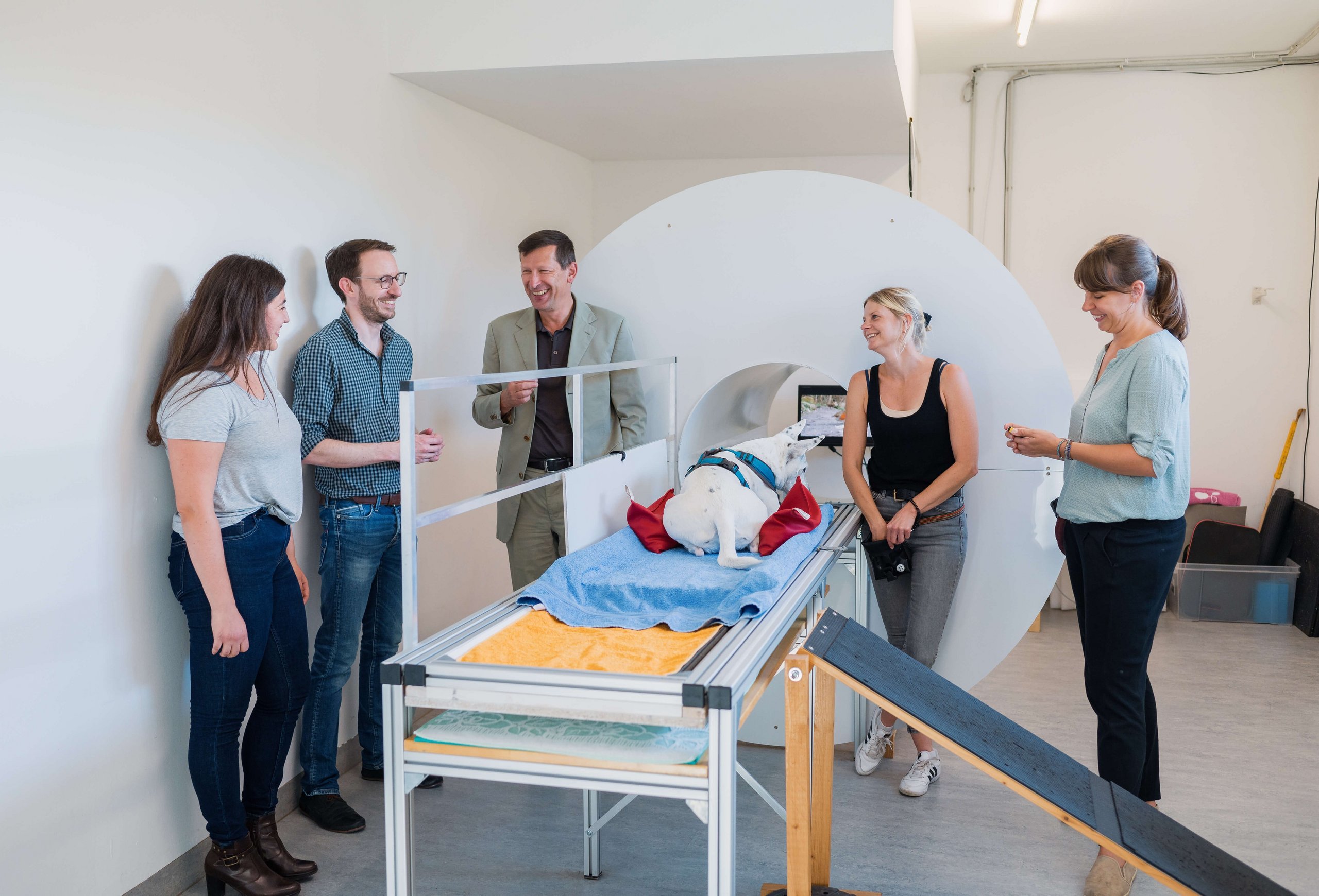Several people from the project team are standing in front of the replica scanner, a dog is lying on the MRI table.