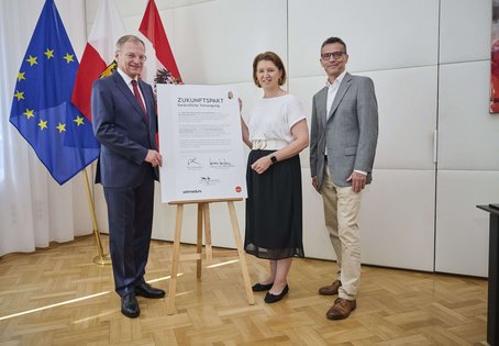 3 Personen mit Urkunde vor Flaggen